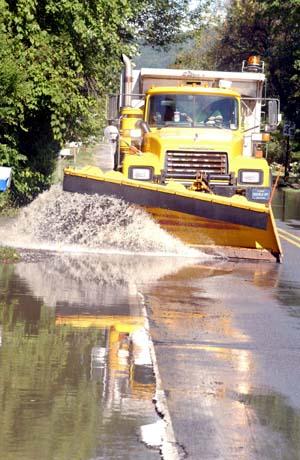 Connie Holt uses a plow to clear water and debris from a roadway in Milesburg.